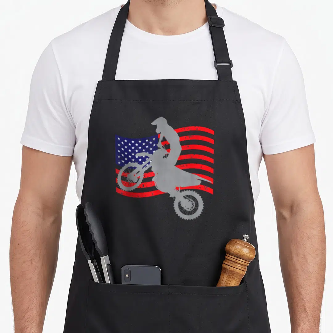 Dirt youth bike apron - White motocross rider silhouette on distressed red white and blue flag — shown on a black cotton canvas apron against a white background