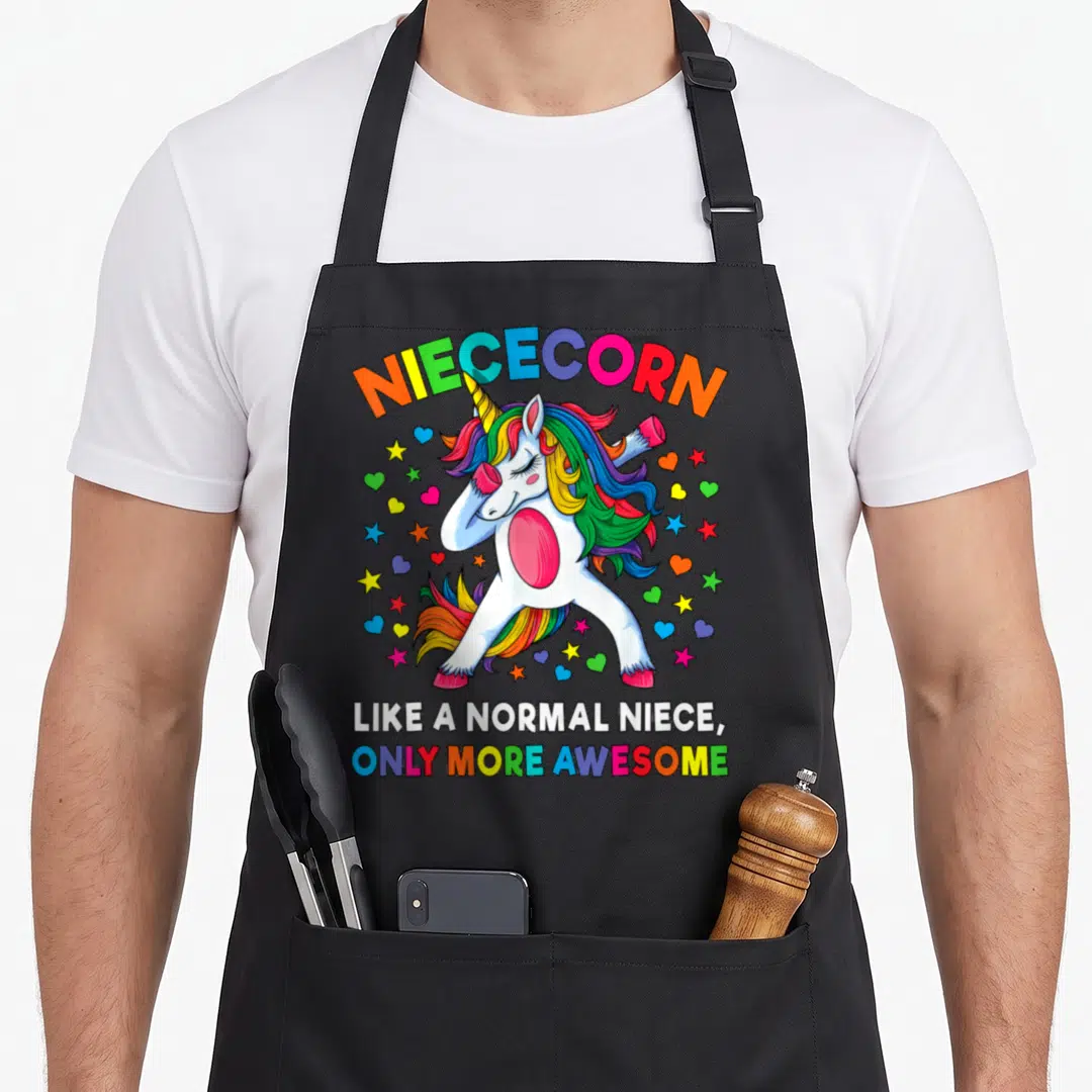 Niececorn unicorn apron - White cartoon unicorn dabbing with rainbow mane surrounded by stars and hearts — shown on a black cotton canvas apron against a white background