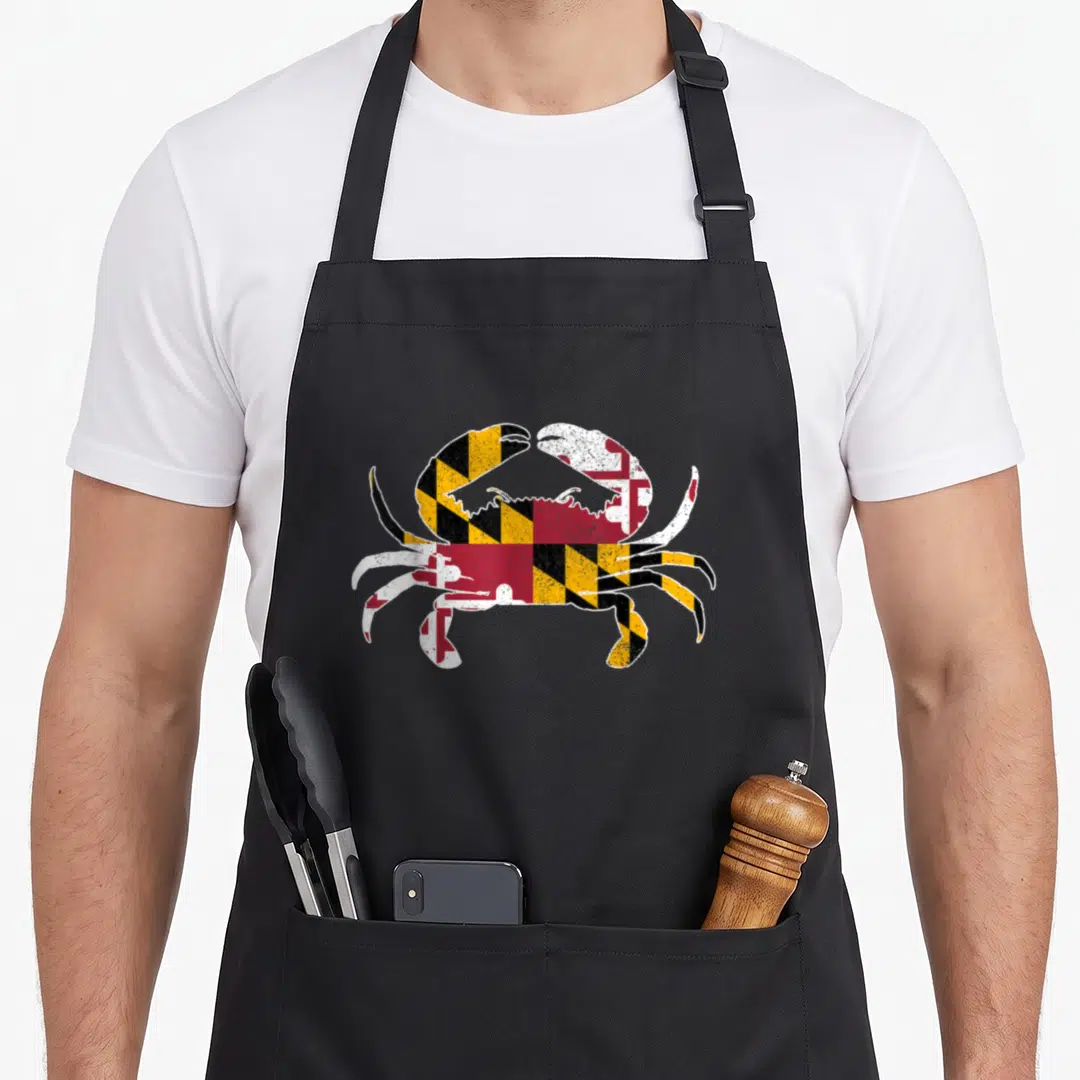 Blue flag crab apron - Distressed crab silhouette filled with red white black and yellow geometric flag pattern — shown on a black cotton canvas apron against a white background