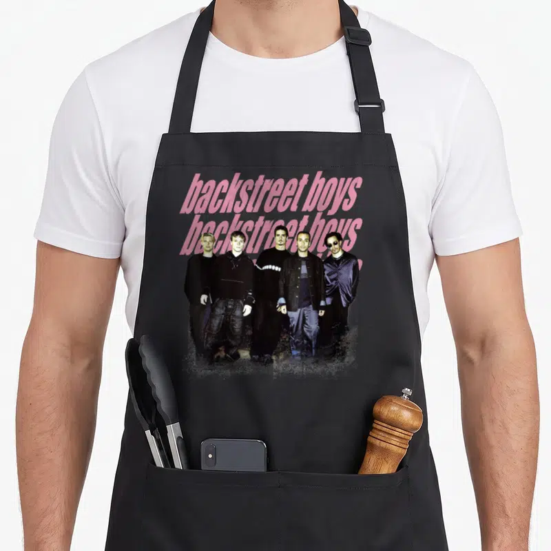 Backstreet dark grey apron - Five men standing in a row behind two lines of pink script text on a grey background — shown on a black cotton canvas apron against a white background