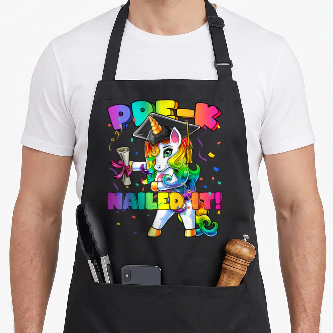 Flossing pre unicorn apron - Cartoon unicorn with rainbow mane wearing graduation cap holding diploma with PRE-K Nailed — shown on a black cotton canvas apron against a white background