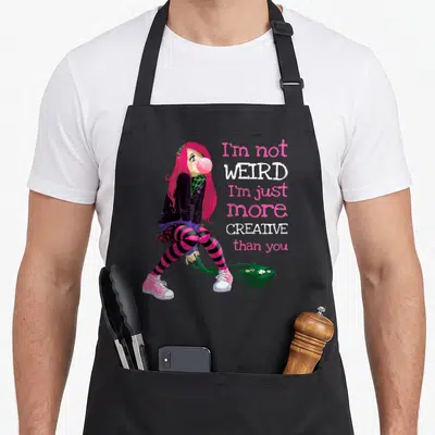Anime goth apron - Cartoon girl with pink hair and striped tights beside stacked text I'm not weird I'm just more — shown on a black cotton canvas apron against a white background