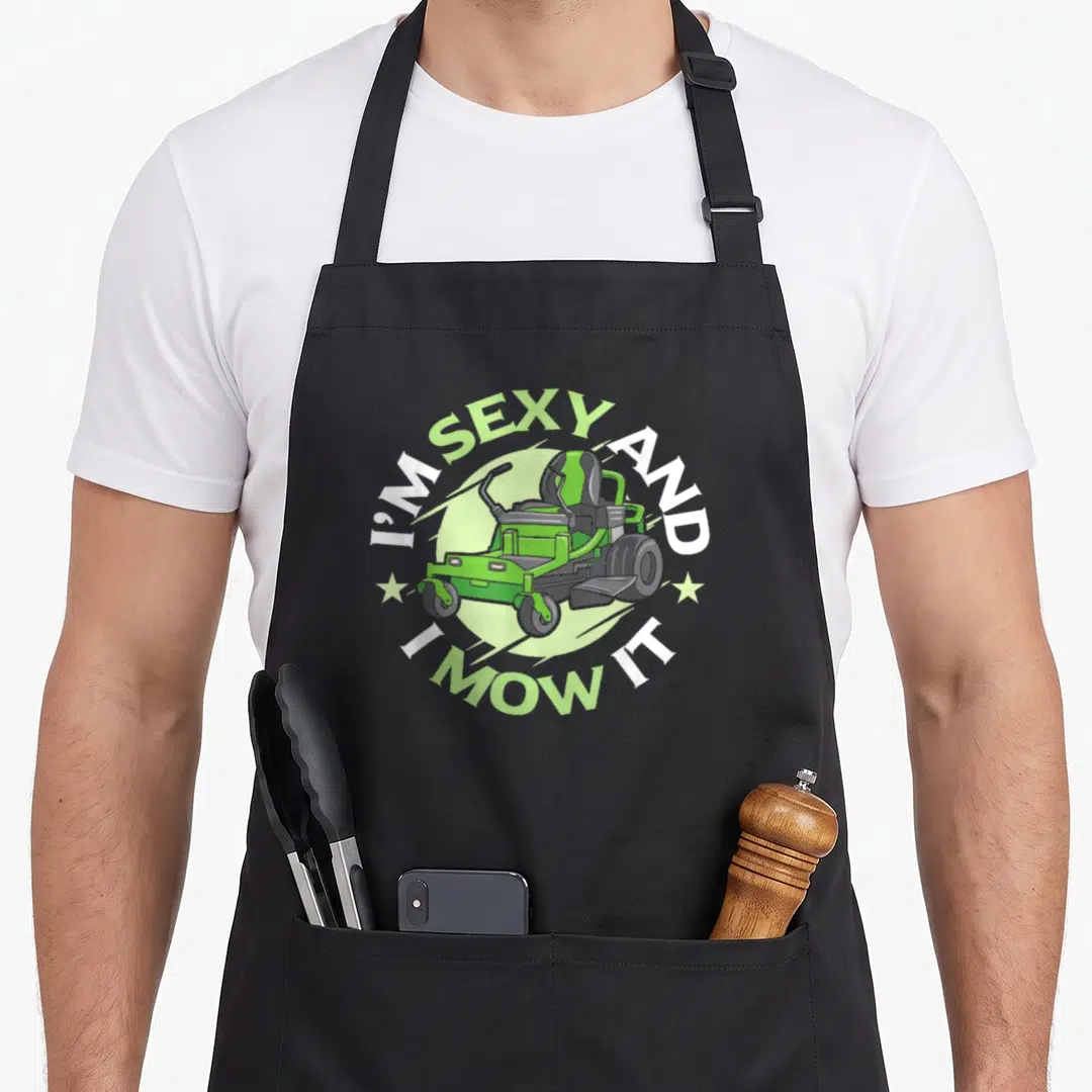 Mow service apron - Green riding mower in circle with I'M SEXY AND, I MOW IT text and two stars — shown on a black cotton canvas apron against a white background