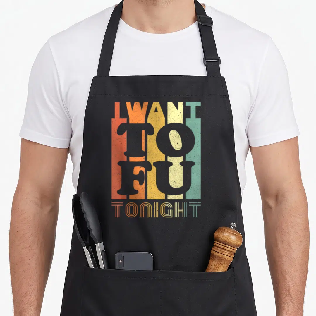 Tofu vegan apron - I WANT TO FU TONIGHT text over vertical orange yellow beige green grey stripes — shown on a black cotton canvas apron against a white background
