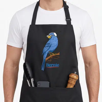 Presidential us aprons - Realistic blue jay wearing glasses perched on a brown branch with Bernie text below — shown on a black cotton canvas apron against a white background