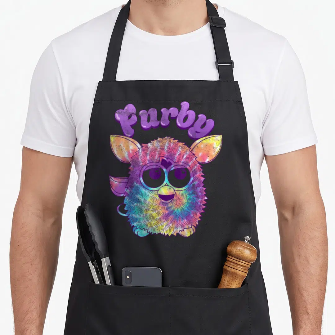Dyed tie apron - Arched purple furby text above a multi-colored cartoon robot face with fuzzy texture — shown on a black cotton canvas apron against a white background