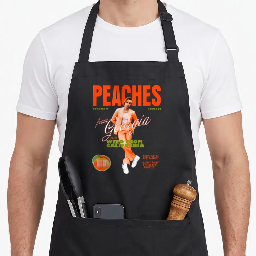 Justin peaches apron - Man in orange suit magazine cover design with barcode peach and bold typography — shown on a black cotton canvas apron against a white background