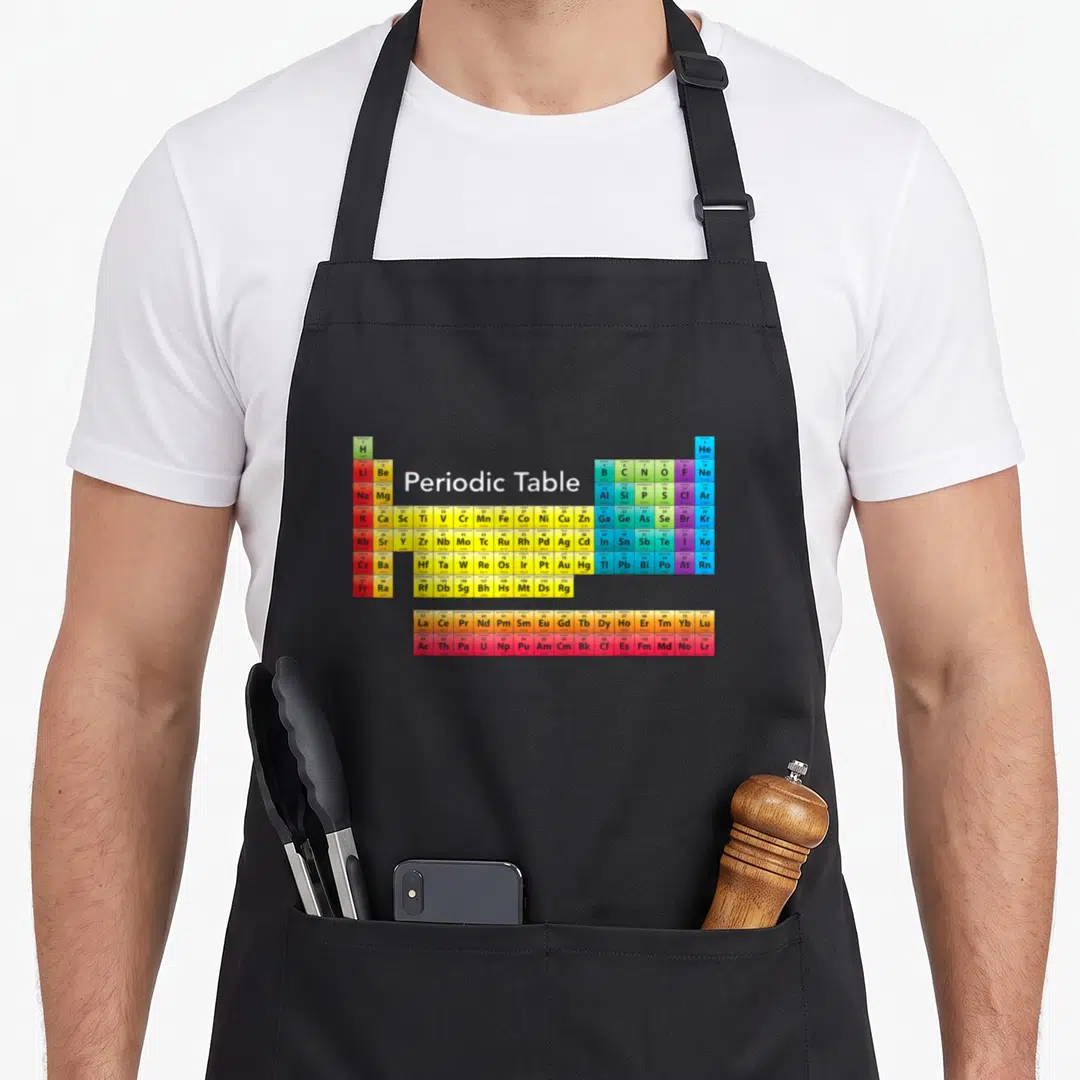 Coded table apron - Multicolored periodic table grid with centered white text Periodic Table — shown on a black cotton canvas apron against a white background
