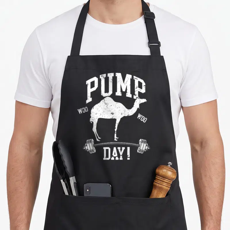 Pump training apron - White distressed camel silhouette on barbell with PUMP WOO WOO DAY! text — shown on a black cotton canvas apron against a white background
