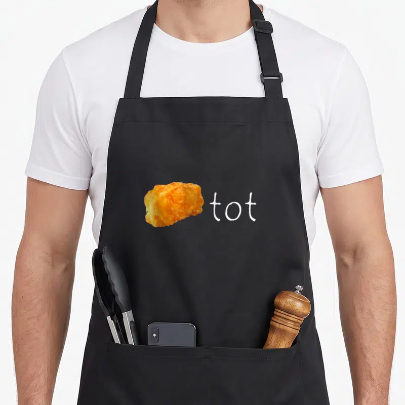 Tot potato apron - Orange tater tot photo next to white lowercase word tot — shown on a black cotton canvas apron against a white background