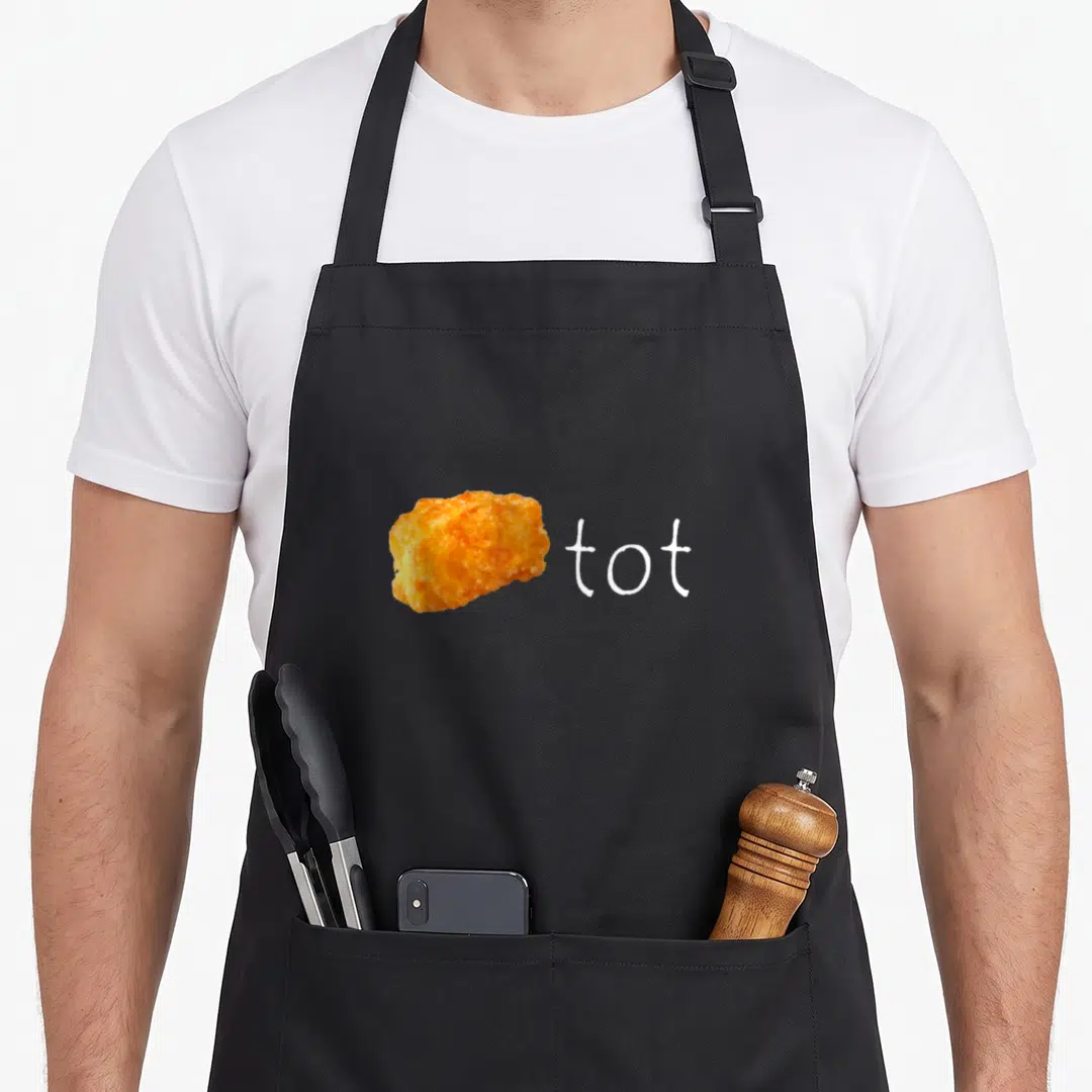 Tot potato apron - Orange tater tot photo next to white lowercase word tot — shown on a black cotton canvas apron against a white background