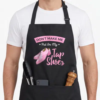 Tap shoe apron - Pink cartoon tap shoes with banner reading Don't Make Me Put On My Tap Shoes — shown on a black cotton canvas apron against a white background