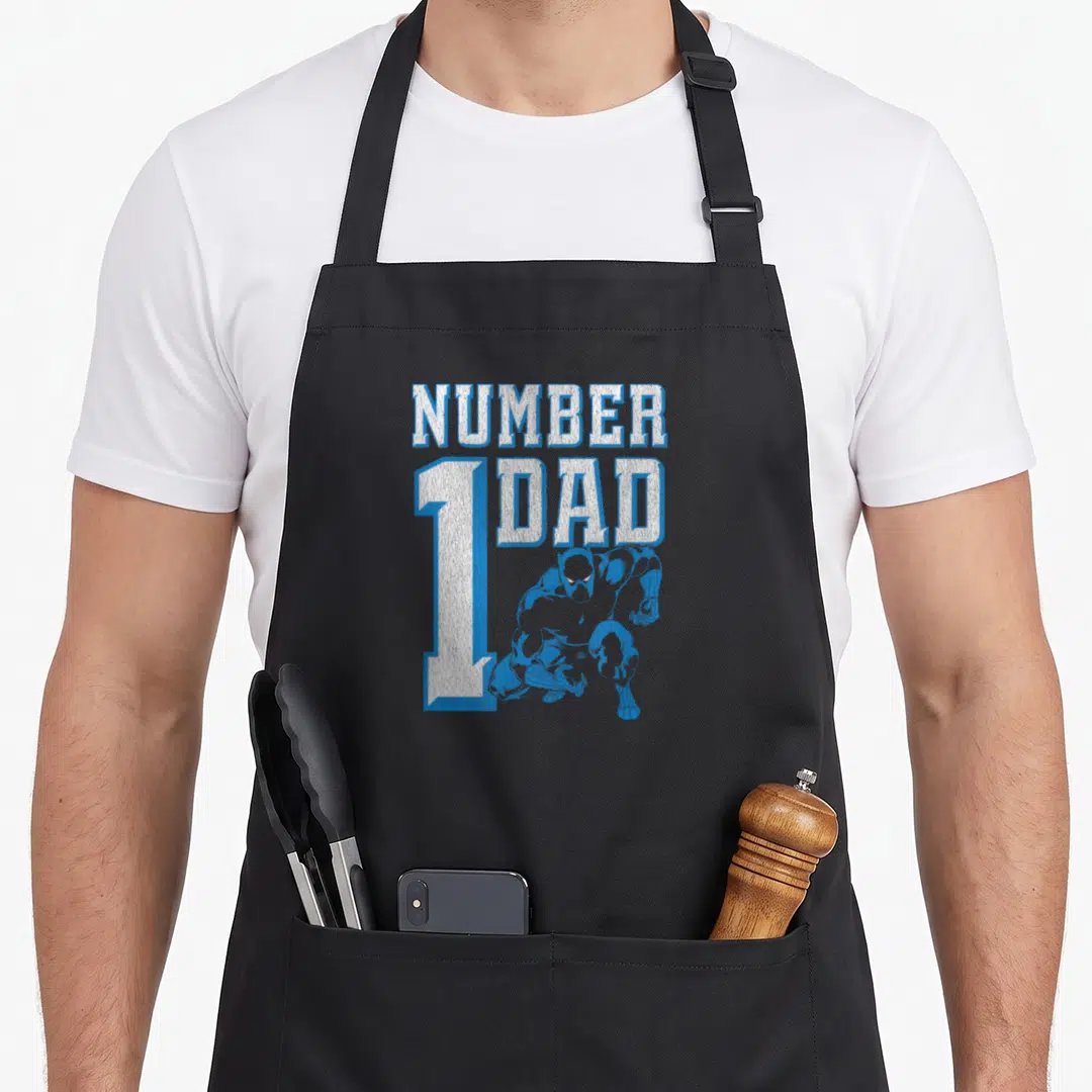 Number black dad apron - Blue superhero crouching in front of white and blue text reading NUMBER 1 DAD — shown on a black cotton canvas apron against a white background
