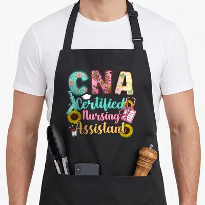 Certified assistant nursing aprons - CNA text with floral patterns, syringe, stethoscope, sunflowers, and stacked title — shown on a black cotton canvas apron against a white background