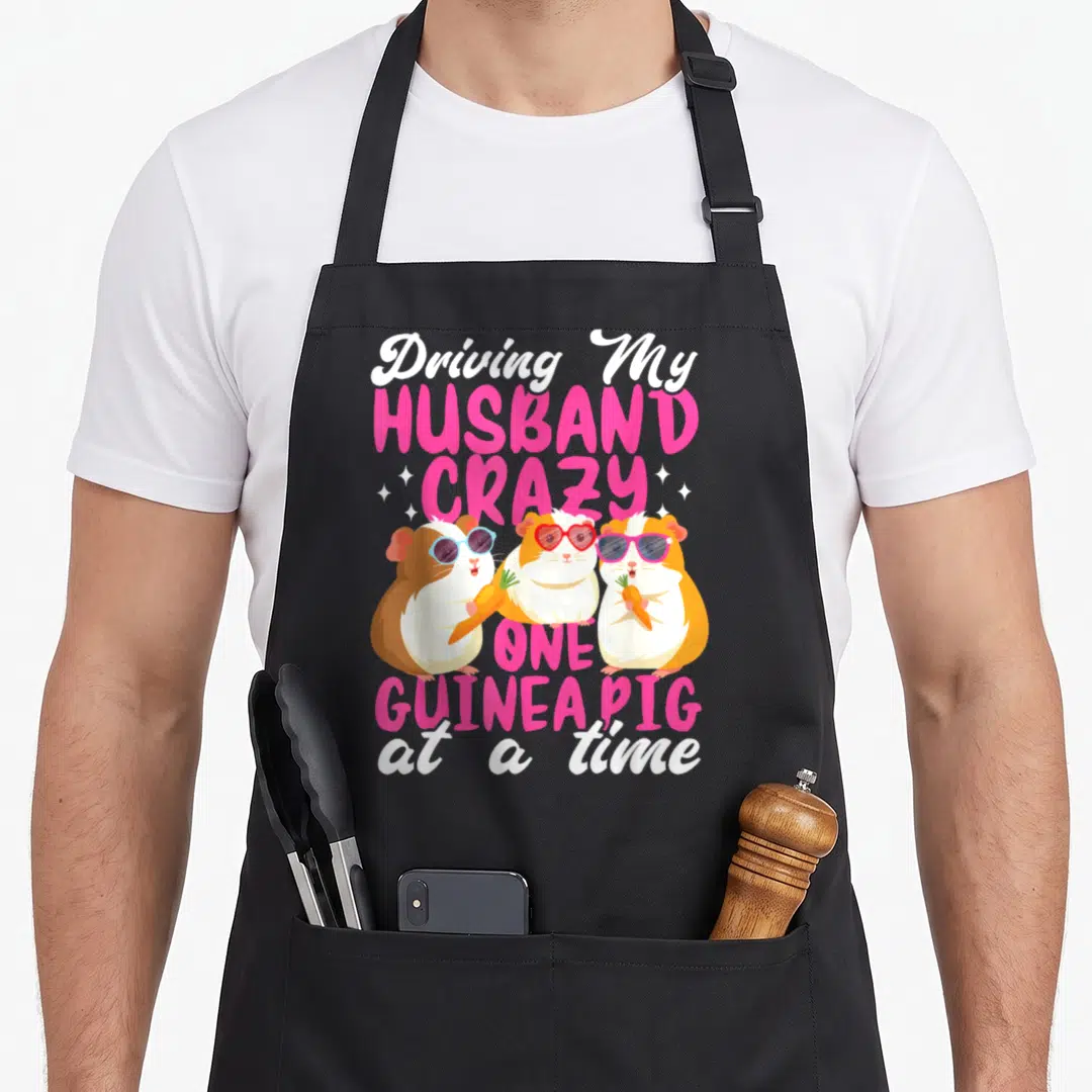 Driving husband wife aprons - Three cartoon guinea pigs with sunglasses holding carrots under stacked pink and white — shown on a black cotton canvas apron against a white background
