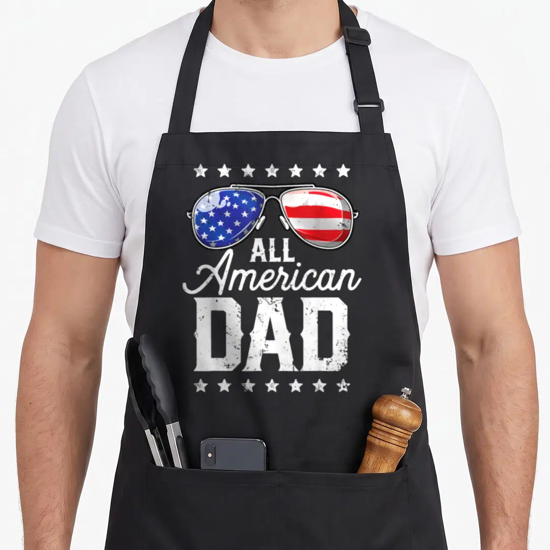 4th father day apron - Distressed aviator sunglasses with flag lenses and All American DAD text framed by two rows — shown on a black cotton canvas apron against a white background