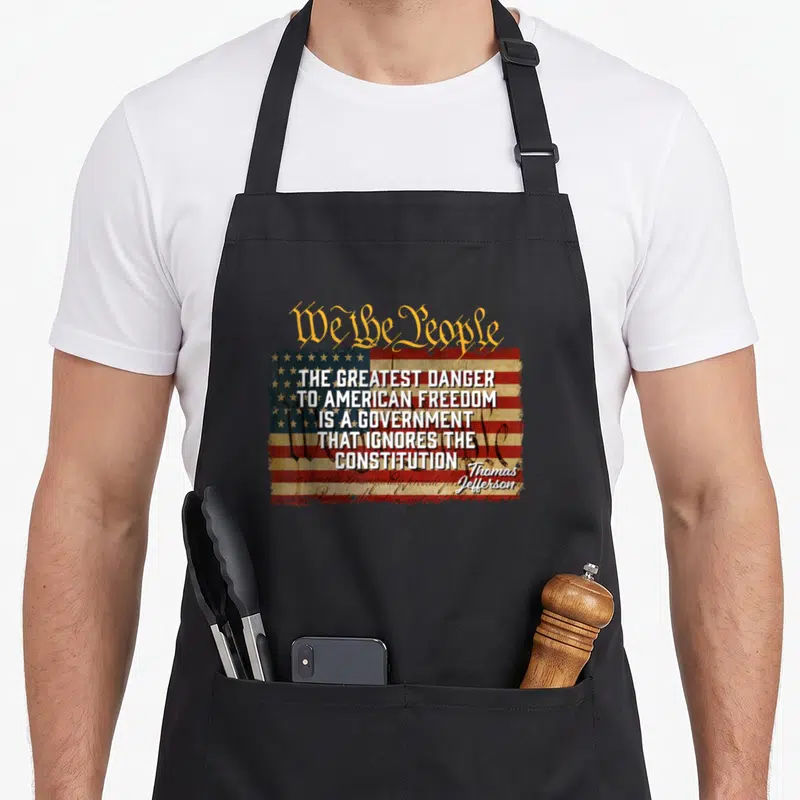 Greatest mount jefferson apron - Distressed US flag with We the People text and Thomas Jefferson quote about government — shown on a black cotton canvas apron against a white background