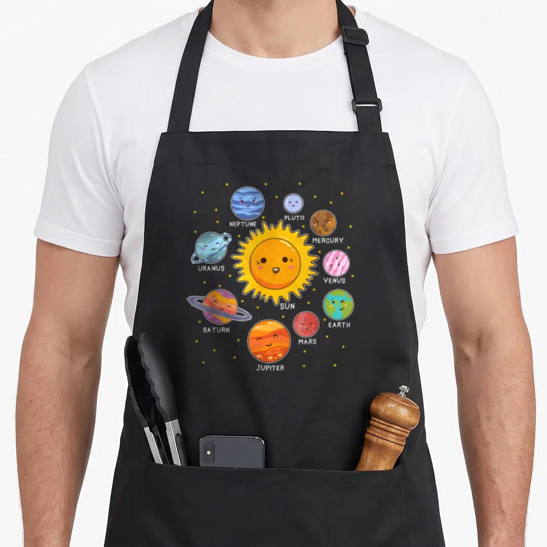 System space planets apron - Cartoon sun and nine labeled planets arranged in a circle with small yellow stars — shown on a black cotton canvas apron against a white background
