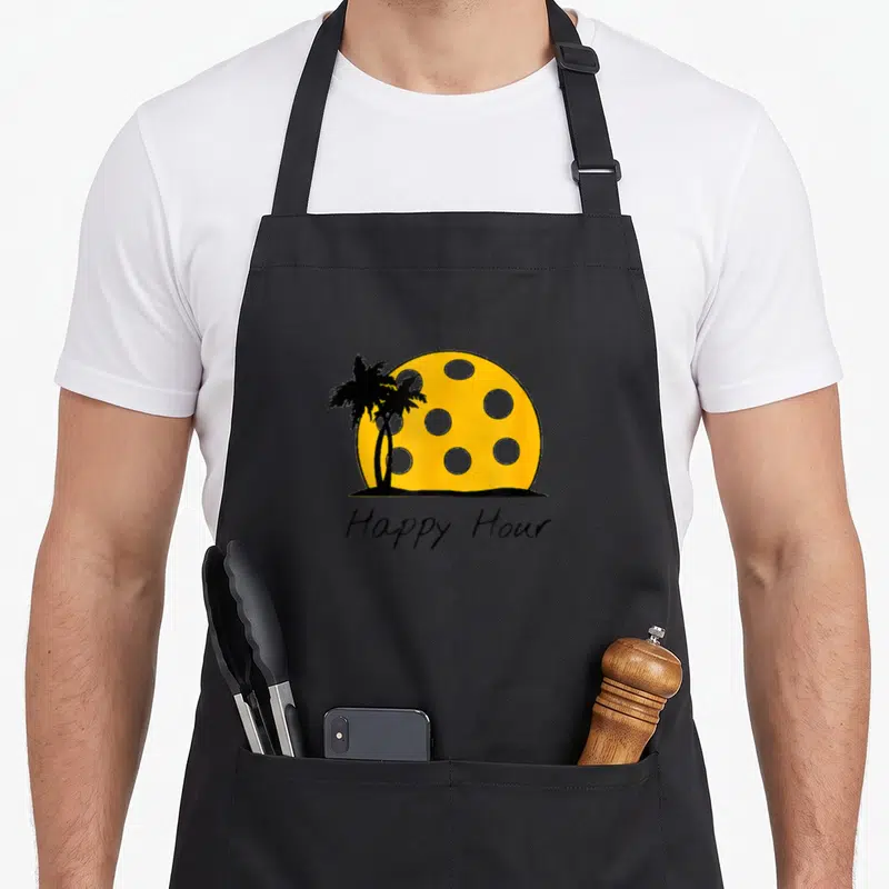 Hour pickleball apron - Yellow cheese sun with black palm trees and Happy Hour text — shown on a black cotton canvas apron against a white background