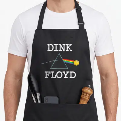 Dink pickleball apron - DINK FLOYD text with prism and rainbow hitting yellow pickleball — shown on a black cotton canvas apron against a white background