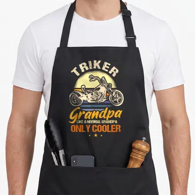 Triker grandad aprons - Retro white trike on yellow sun with orange stripes and grandpa text — shown on a black cotton canvas apron against a white background