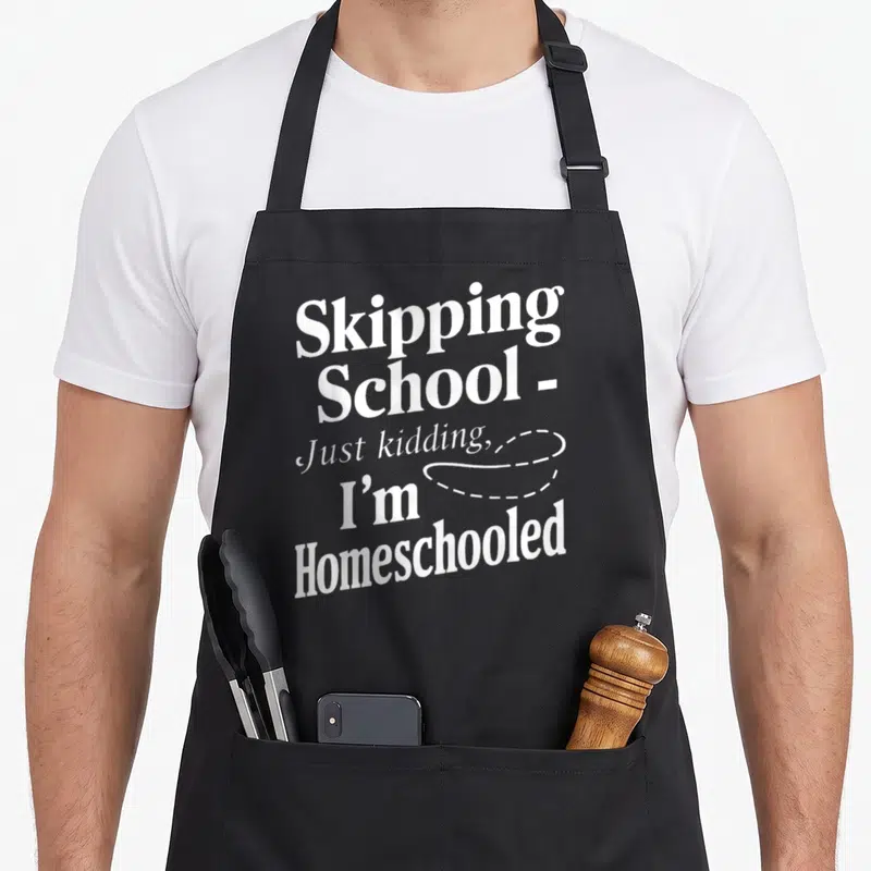 Funny homeschool personalized teacher apron - Stacked white text reading Skipping School Just kidding I'm Homeschooled — shown on a black cotton canvas apron against a white background