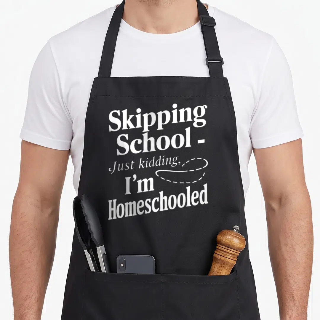 Funny homeschool personalized teacher apron - Stacked white text reading Skipping School Just kidding I'm Homeschooled — shown on a black cotton canvas apron against a white background