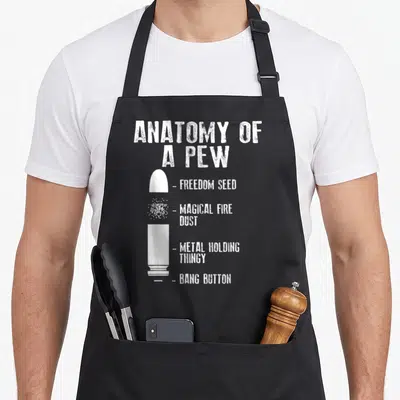 Weapon anatomy apron - White disassembled bullet diagram labeled Bang Button and Freedom Seed in distressed typography — shown on a black cotton canvas apron against a white background