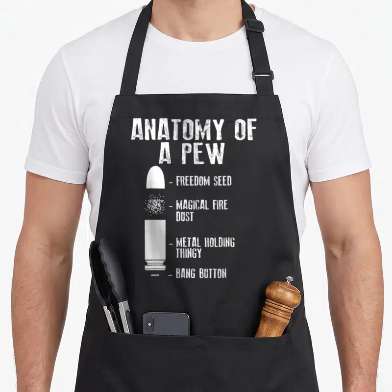 Weapon anatomy apron - White disassembled bullet diagram labeled Bang Button and Freedom Seed in distressed typography — shown on a black cotton canvas apron against a white background