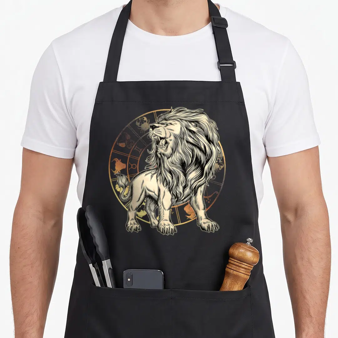 Zodiac birthday apron - Line art roaring lion over gold zodiac wheel on black fabric — shown on a black cotton canvas apron against a white background