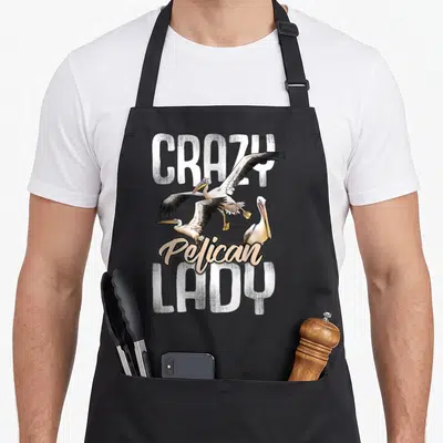 Pelican watching bird apron - Three pelicans flying over script text framed by distressed block letters — shown on a black cotton canvas apron against a white background