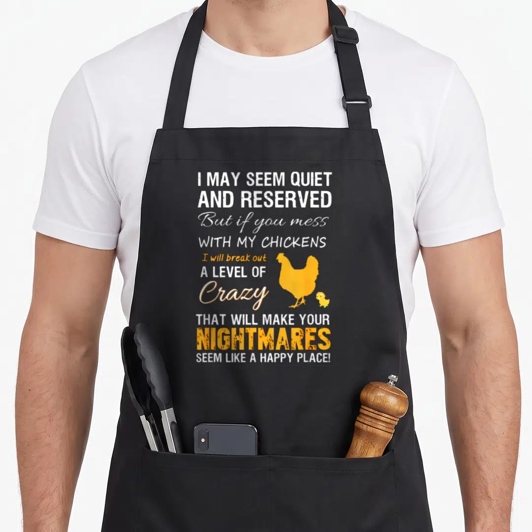 Funny farmer chicken apron - White and yellow text warning about protecting chickens with hen and chick silhouettes — shown on a black cotton canvas apron against a white background