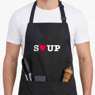 Cute soup lovers apron - White SOUP text with red heart replacing the letter O — shown on a black cotton canvas apron against a white background