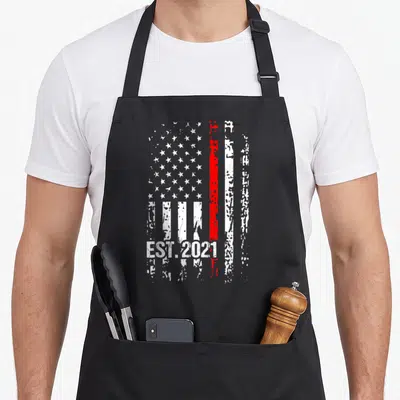 Graduation firefighter apron - Vertical distressed American flag with thin red line and EST.2021 text at bottom — shown on a black cotton canvas apron against a white background