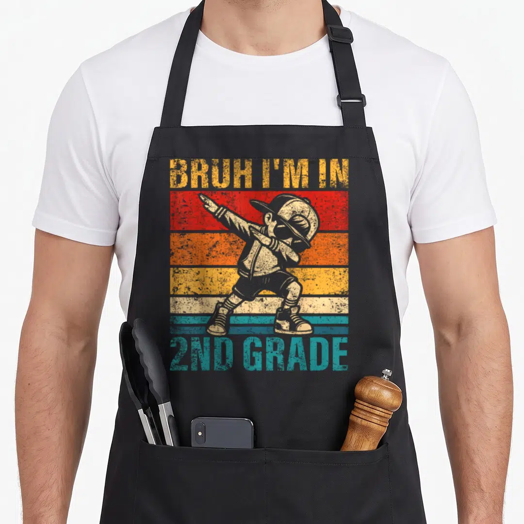 Dabbing 2nd apron - Grey dabbing child silhouette over red orange yellow blue grey stripes with BRUH I'M IN 2ND GRADE — shown on a black cotton canvas apron against a white background