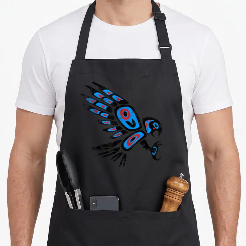 Tailed native american apron - Stylized black, blue, and red tribal bird in flight with spread wings — shown on a black cotton canvas apron against a white background