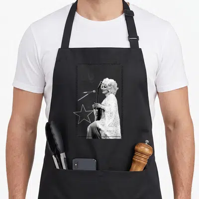 Dolly country apron - Dolly Parton guitar photo with COUNTRY MUSIC LEGEND text, large star, and musical notes — shown on a black cotton canvas apron against a white background