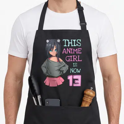 Cute birthday anime mom apron - Anime girl with cat ears next to stacked text 'THIS ANIME GIRL IS NOW 13' in pink — shown on a black cotton canvas apron against a white background