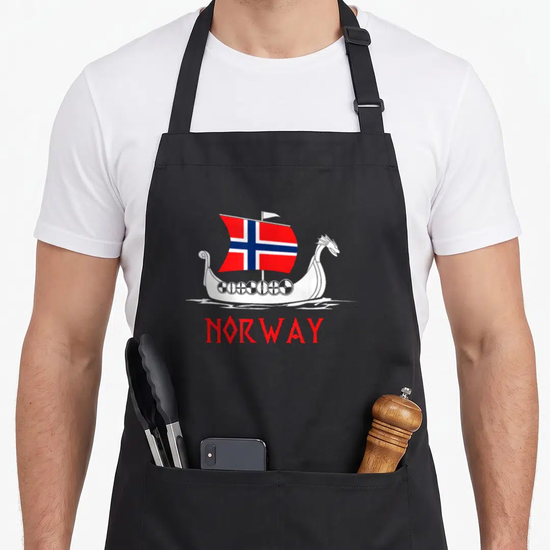 Viking norwegian kitchen aprons - Viking ship with Norwegian flag and NORWAY text in red white blue cartoon style — shown on a black cotton canvas apron against a white background