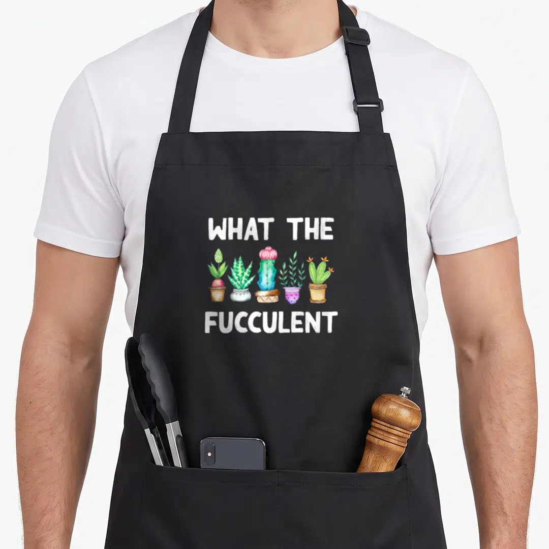 Succulent cactus apron - Five potted succulents in watercolor between white text reading WHAT THE FUCCULENT — shown on a black cotton canvas apron against a white background