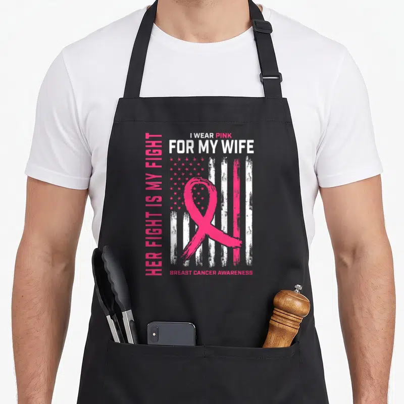 Breast wife apron - Distressed pink ribbon over faded flag with text I Wear Pink For My Wife — shown on a black cotton canvas apron against a white background