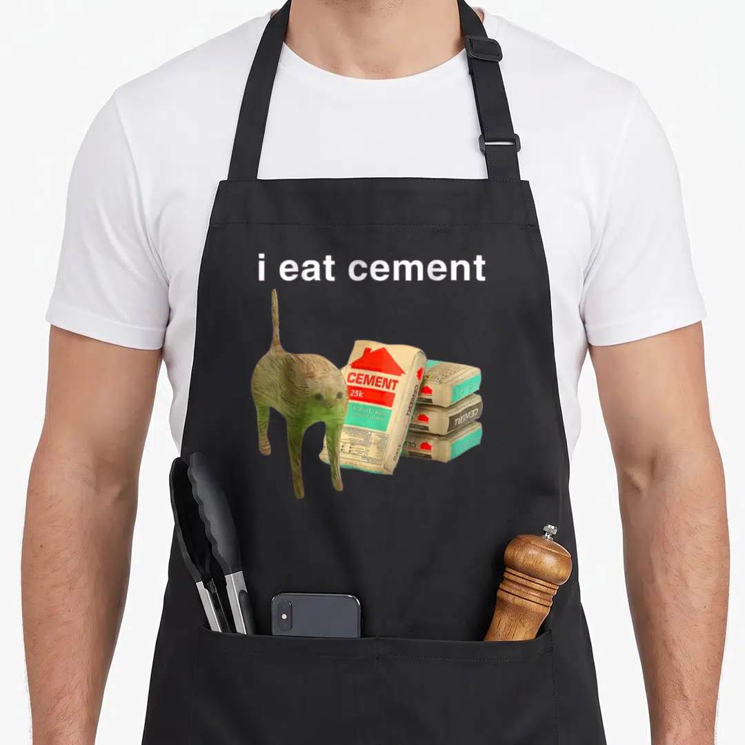 Cement cat apron - Cartoon cat standing next to cement bags with i eat cement text — shown on a black cotton canvas apron against a white background