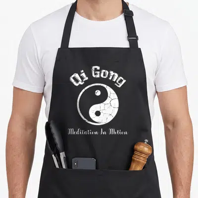 Qigong apron or apron - Distressed white yin yang with arched Qi Gong text and centered Meditation In Motion caption — shown on a black cotton canvas apron against a white background