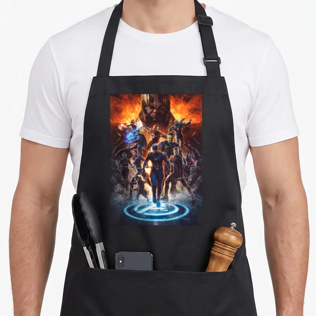 Endgame earth apron - Thanos head looms above Avengers heroes with logo at bottom in orange and blue photo style — shown on a black cotton canvas apron against a white background