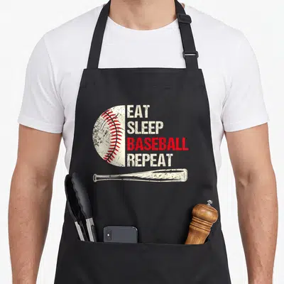 Sleep repeat baseball apron - EAT SLEEP BASEBALL REPEAT text with white ball and bat on distressed background — shown on a black cotton canvas apron against a white background
