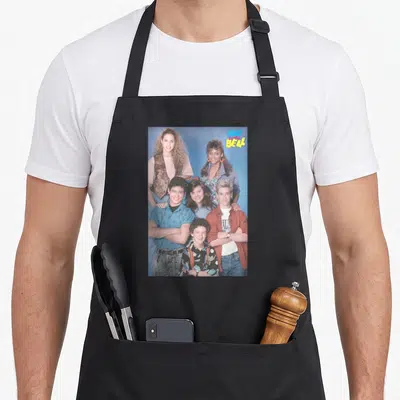 Saved novelty apron - Six people group photo blue background SAVED THE BELL logo pink yellow — shown on a black cotton canvas apron against a white background