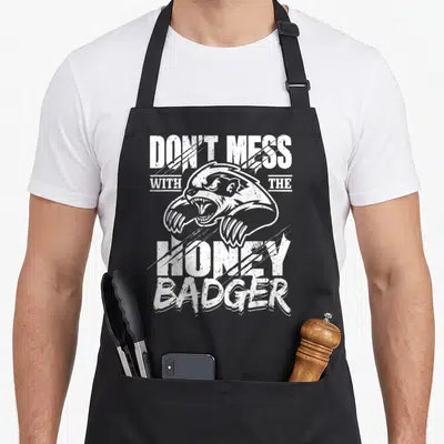 Mess badger apron - White distressed honey badger head and text DON'T MESS WITH THE HONEY BADGER on black fabric — shown on a black cotton canvas apron against a white background