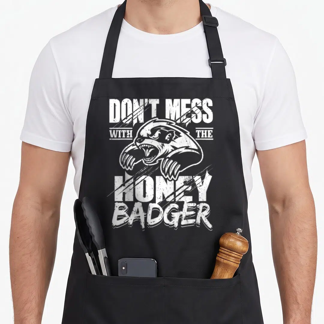 Mess badger apron - White distressed honey badger head and text DON'T MESS WITH THE HONEY BADGER on black fabric — shown on a black cotton canvas apron against a white background