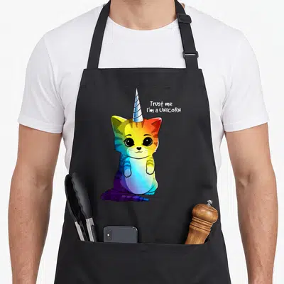 Caticorn unicorn apron - Rainbow cat with unicorn horn and text Trust me I'm a unicorn — shown on a black cotton canvas apron against a white background